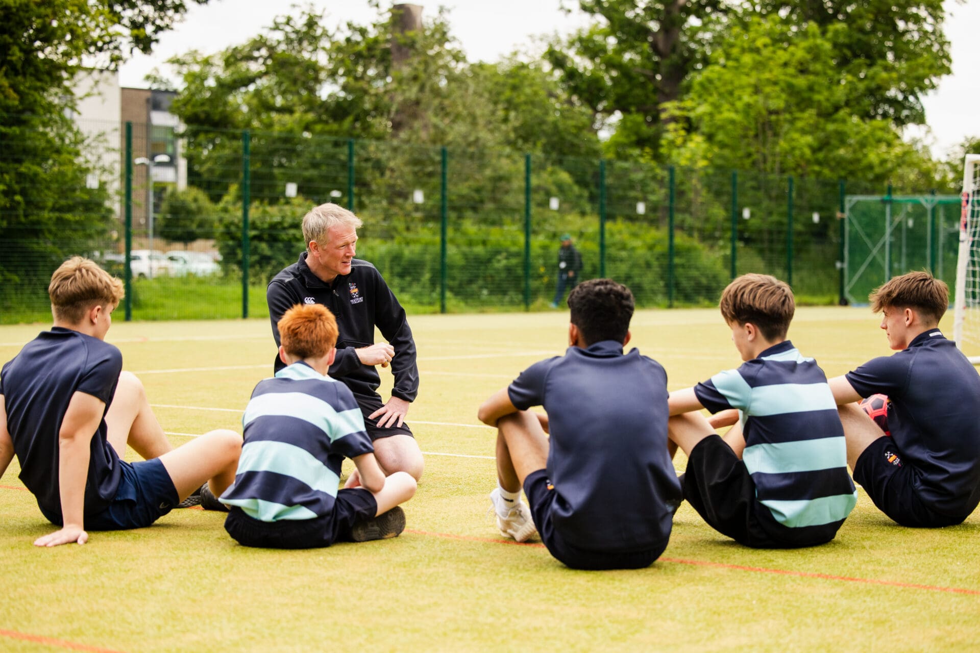 Image of the school head coaching football with a group of students